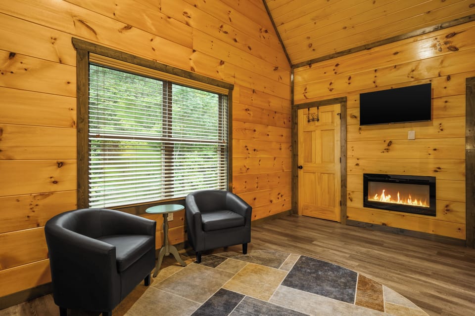 Cozy cabin lounge with fireplace, TV, and peaceful forest views