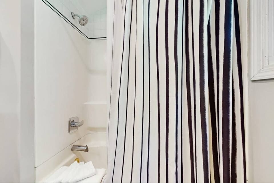 A bathtub and shower combo framed by a black and white striped shower curtain.