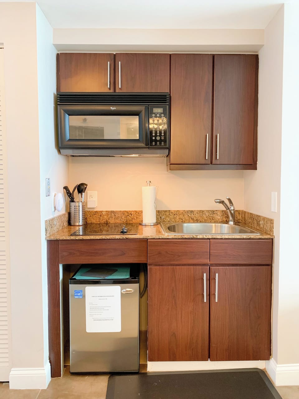 Kitchenette with a stove top and mini fridge, microwave and sink.
