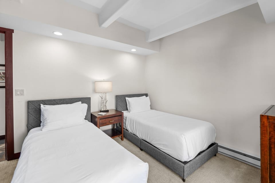 Sink into crisp white linens in your twin bedroom, where exposed beams and warm lighting create the perfect space for peaceful rest.