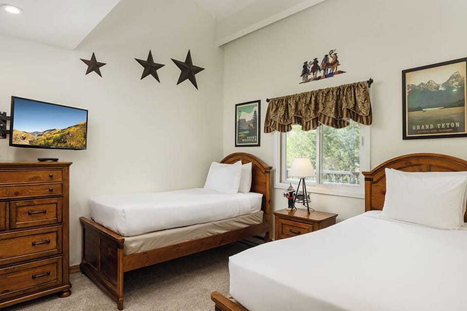 Rest easy in this cozy bedroom with twin beds dressed in crisp white linens. Natural light streams through the window, offering a peaceful view of the surrounding greenery.