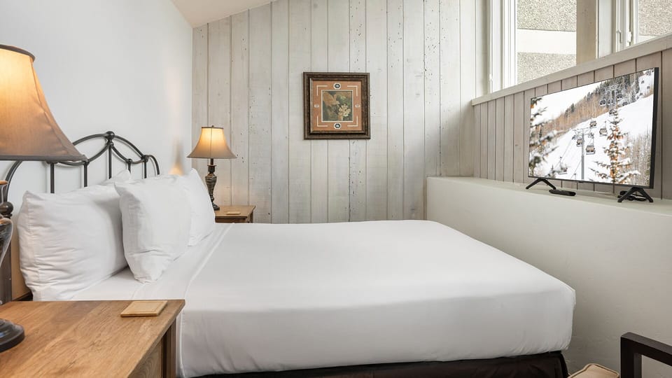 Settle into your cozy haven with crisp white linens, rustic wood-paneled walls, and warm bedside lighting. The bright windows and simple, inviting décor create the perfect retreat after a day exploring the slopes.