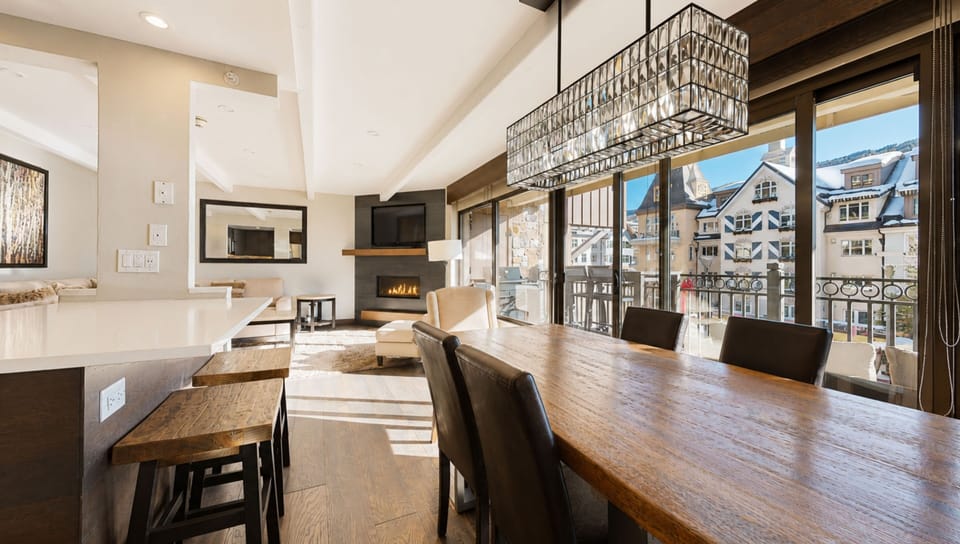 Sunlight streams through expansive windows onto rich wood floors and a cozy fireplace, creating the perfect spot for your mountain retreat. Vaulted ceilings and stunning views of the alpine village complete your ideal escape.