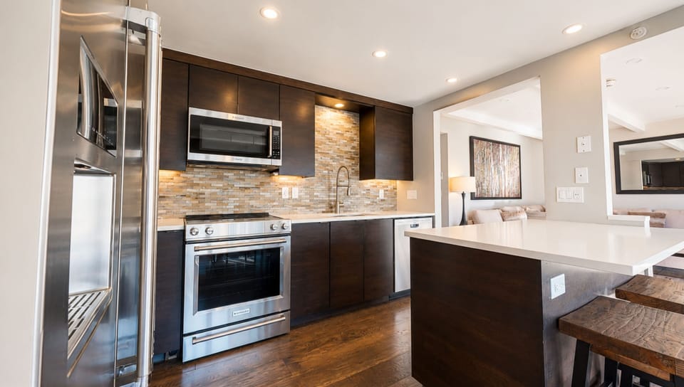 Your gourmet kitchen features sleek dark cabinetry, stone backsplash, stainless steel appliances, and bright countertops—ready for creating memorable meals and easy entertaining.