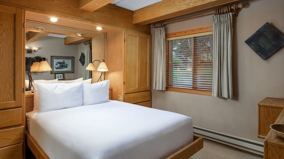 Your inviting bedroom features a plush bed with crisp linens, warm wood accents, and natural light filtering through the window—a peaceful retreat after a day of adventure.