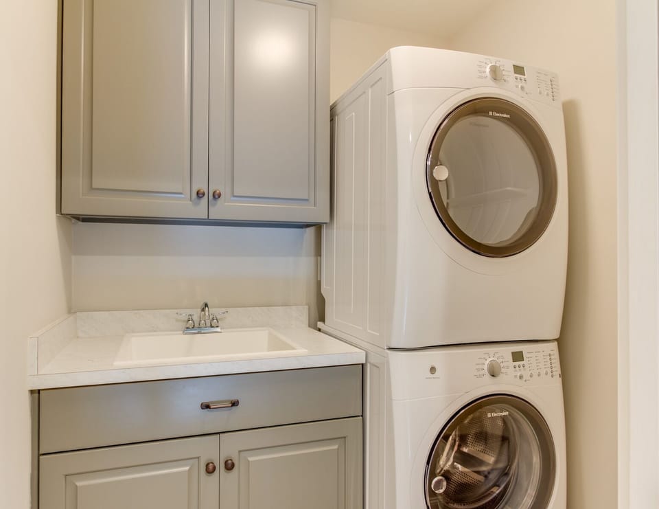 Laundry Room with stacked washer and dryer. There is plenty of folding room and cabinetry for storing cleaning supplies, beach gear, extra towels and anything you might need to tuck away during your visit.