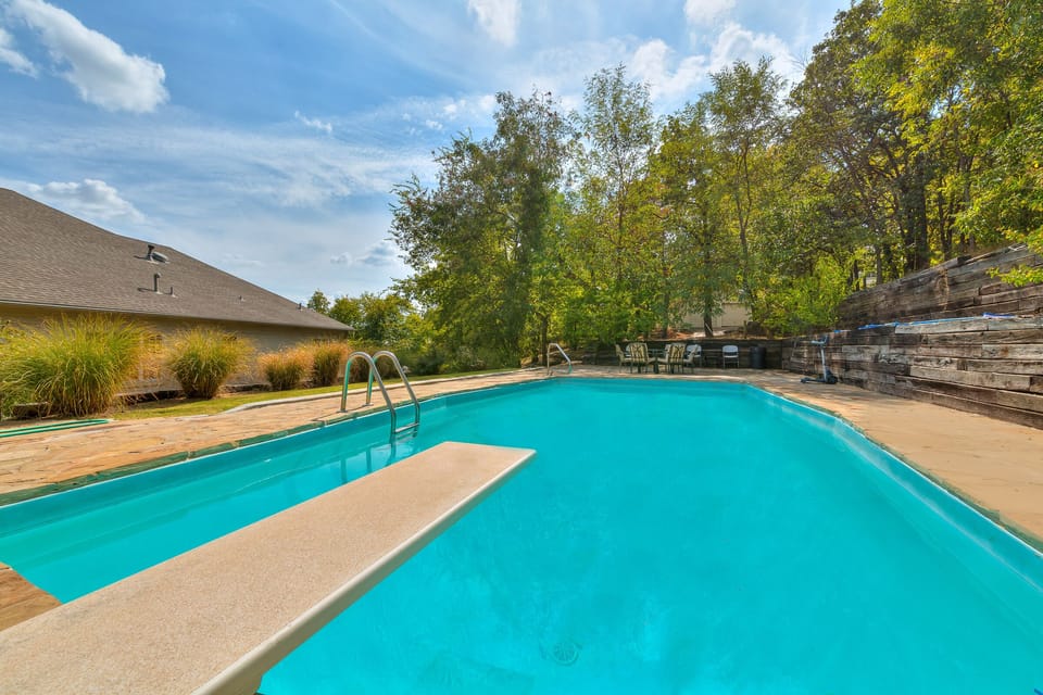 9.5 feet deep heated swimming pool with diving board, surrounded by trees.