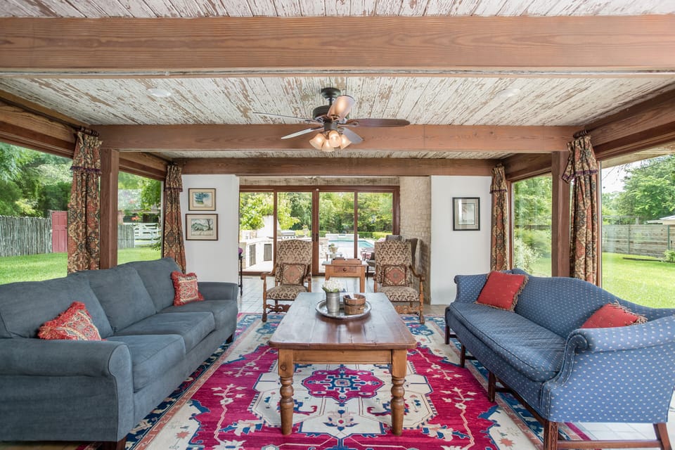 Living room has TV, seating for 10, & floor to ceiling windows onto pool & yard