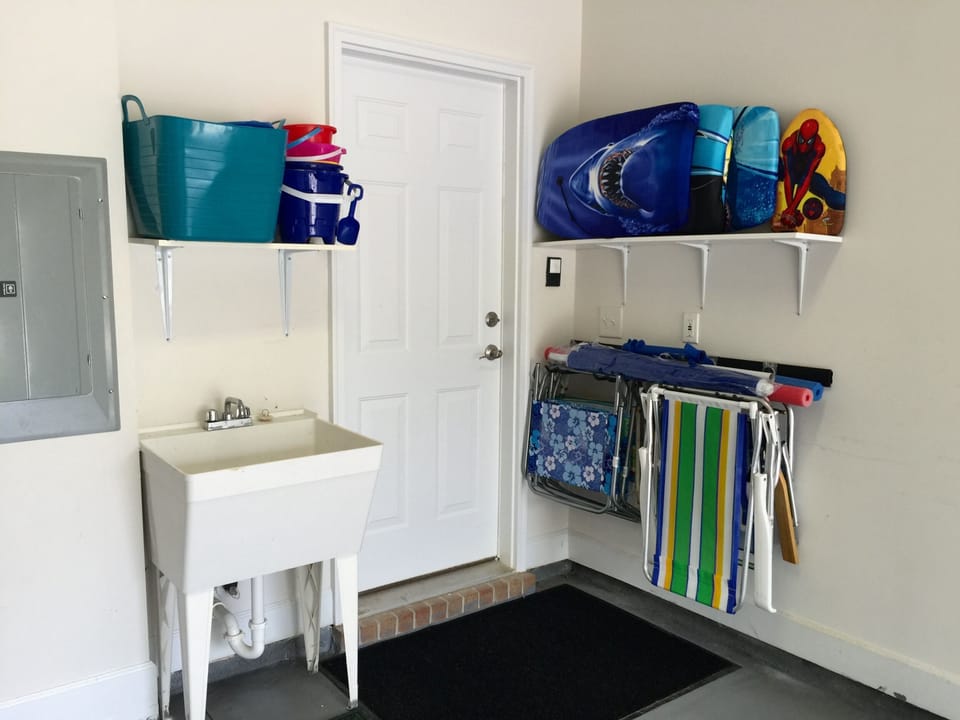 Garage stocked with chairs, umbrella, boogie boards, and beach toys. More inside