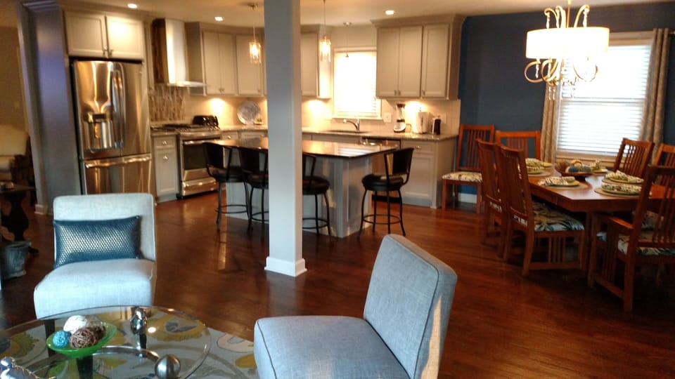 View when walking into house of first living area with armless chairs & kitchen