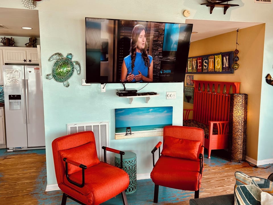 Large smart TV in living room along with two chairs that make out to single beds