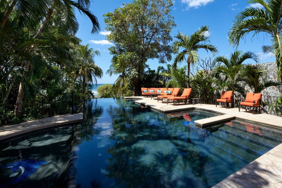 Large, private pool area surrounded by lush vegetation and plush seating. 