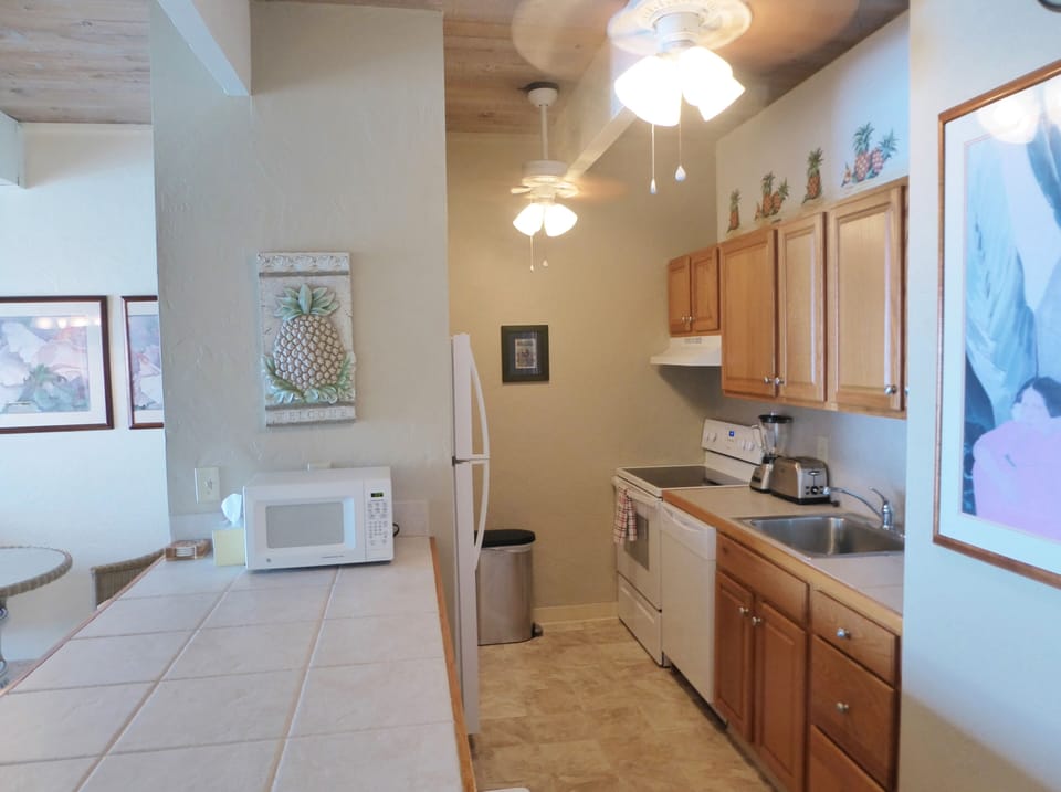 Open kitchen area with large counter with stools and two ceiling fans.