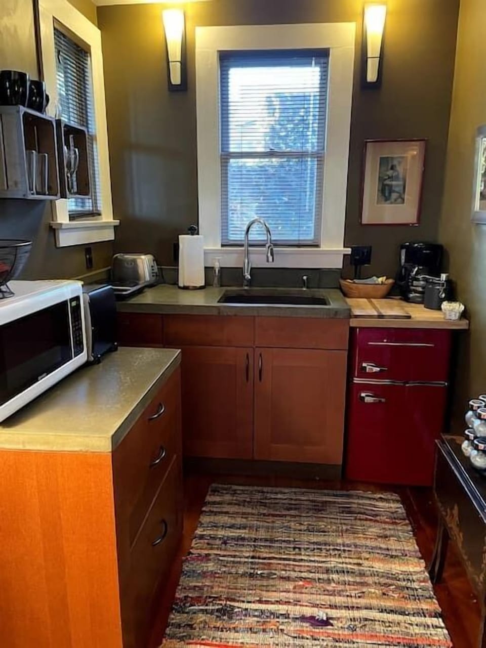 Kitchenette with microwave and toaster oven on top of two drawer stocked cabinet plus one induction hot plate to left of sink and coffee machine on top of mini fridge.