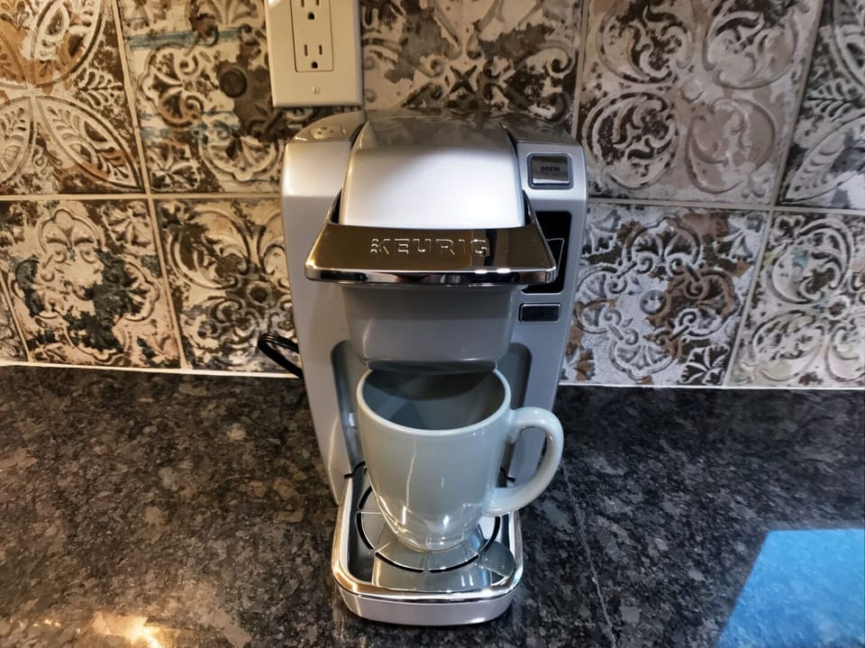 Keurig coffee maker on dark granite countertop with decorative tile backsplash
