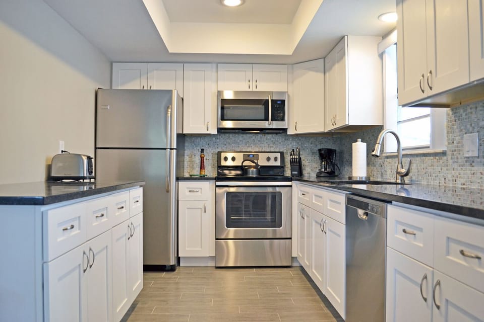 Kitchen with stainless steel appliances, dark countertops, and white cabinetry