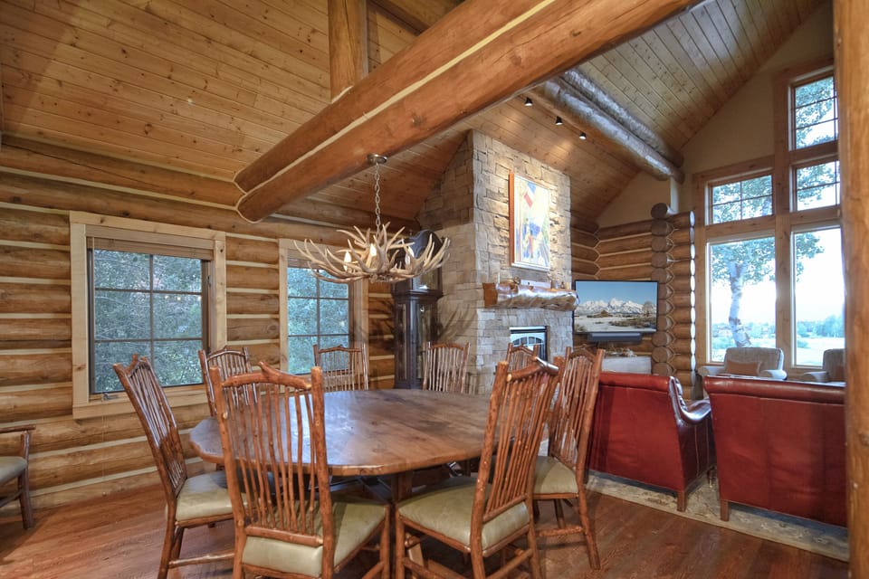 Gather around this stunning rustic dining table where warm wood meets natural stone—you'll love sharing meals by the crackling fireplace under soaring timber beams