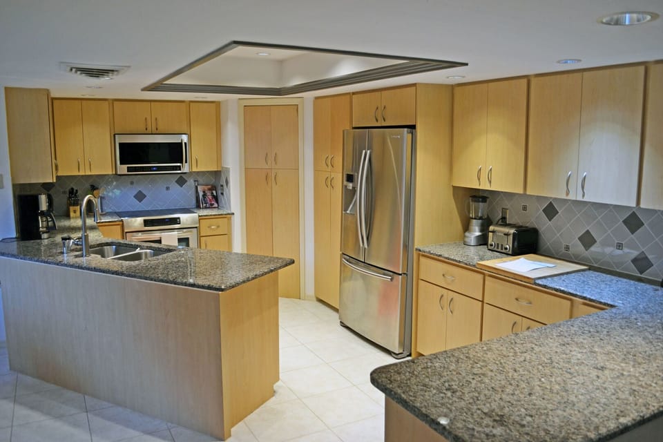 Kitchen with light wood cabinetry, granite island, stainless refrigerator, and tile backsplash