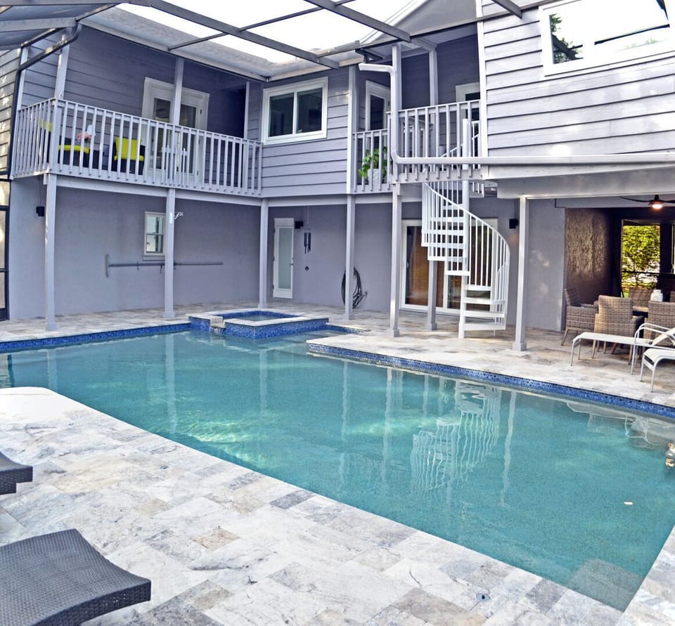 Rear of the two-story home with spiral staircase, pool deck, and screened enclosure