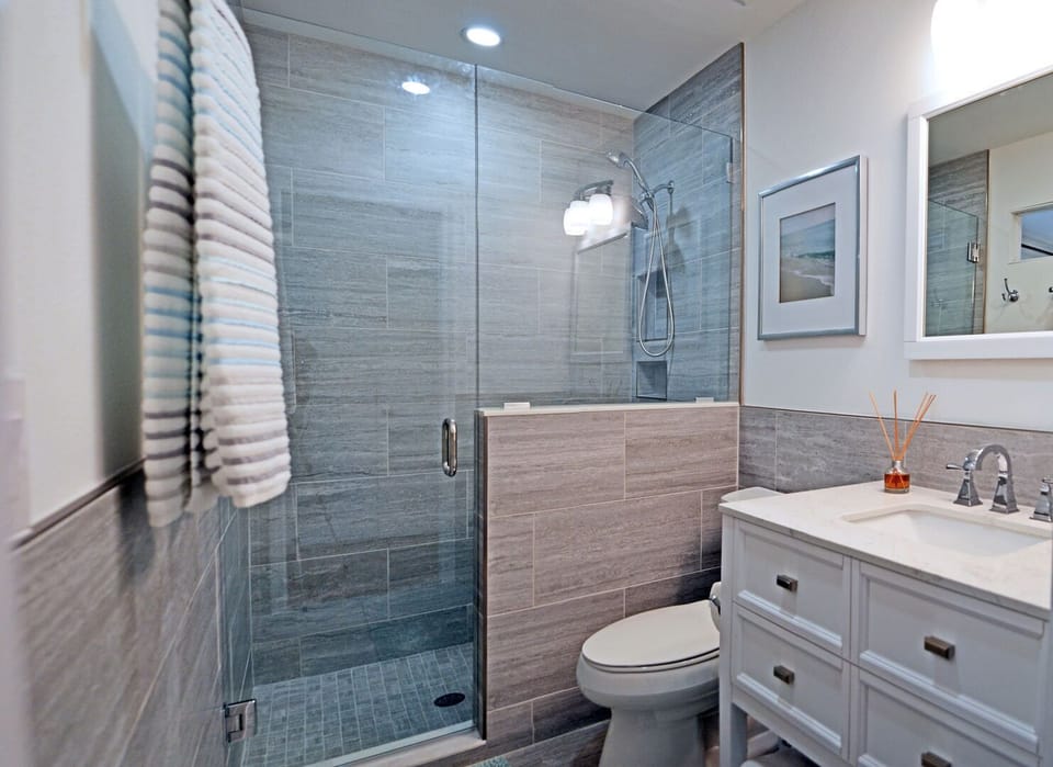 Bathroom with glass walk-in shower featuring gray tile walls, vanity, and coastal art