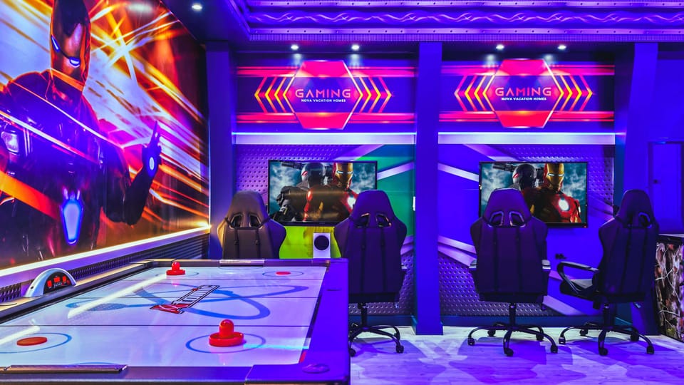 Vibrant gaming room with air hockey table, racing chairs, multiple screens, and superhero-themed decor.
