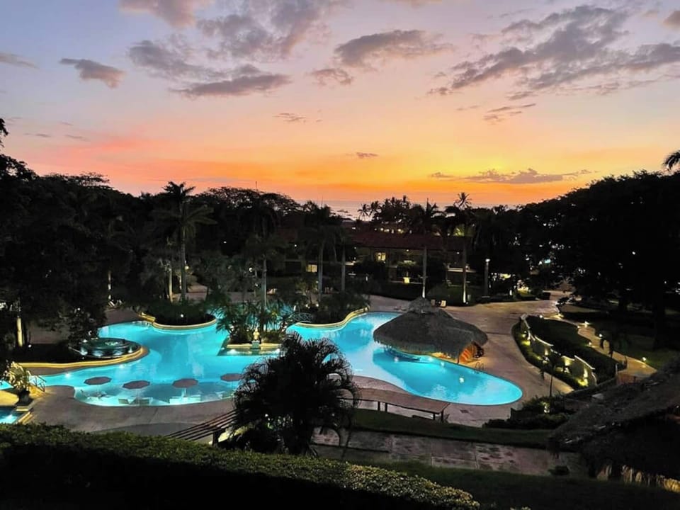 Golden-hour view from the balcony overlooking the resort-style pool, framed by sunset skies and tropical palms. This Tamarindo condo offers unbeatable location, laid-back luxury, and postcard-perfect evenings just steps from the beach.