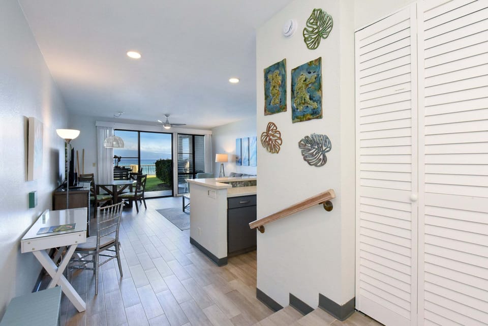 Step inside the unit featuring wall art decor, steps leading down to the open-concept kitchen and sunlit living room with ocean views beyond.