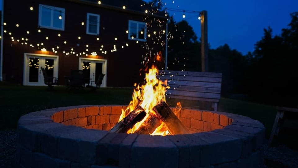 Outdoor fire pit with provided firewood and fire starters, surrounded by flexible seating with benches and chairs. Includes an outdoor dining table, perfect for evening gatherings, outdoor meals, and cozy nights under the stars.