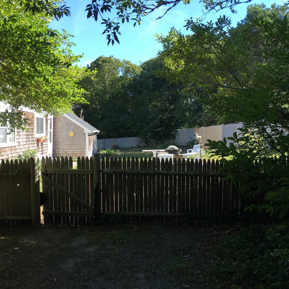 Fenced portion of backyard, includes two picnic tables, grill, and fire pit.
