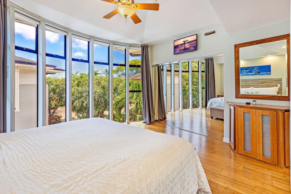 Master bedroom: Wake up in paradise in this bright Maui bedroom with floor-to-ceiling windows and lush tropical views. Relax in comfort with cool bamboo floors, mirrored accents, and a TV for unwinding after sun-filled island adventures. 