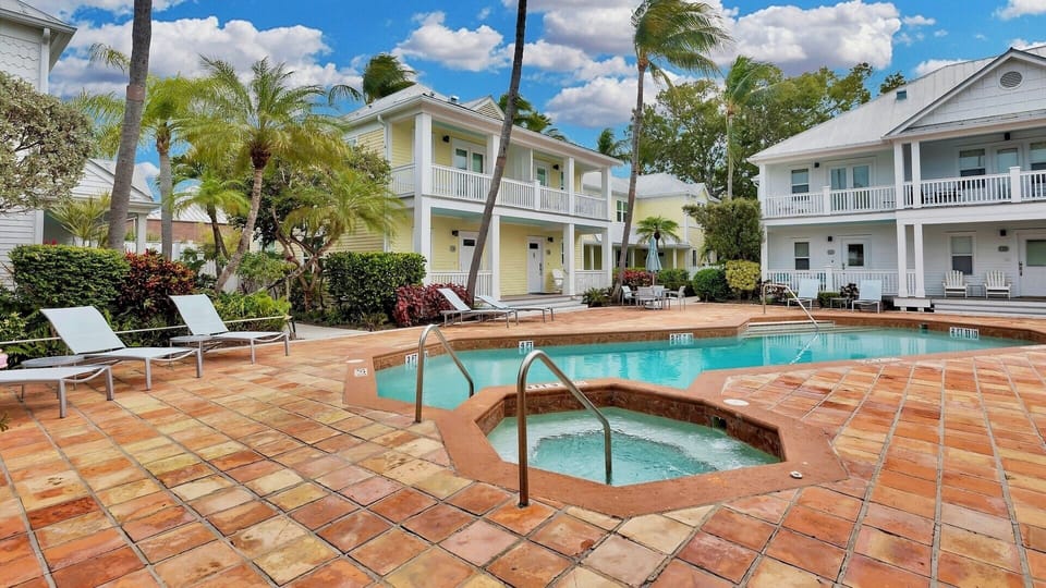 Tropical resort complex with swimming pool, hot tub, and colorful colonial-style buildings surrounded by palm trees.