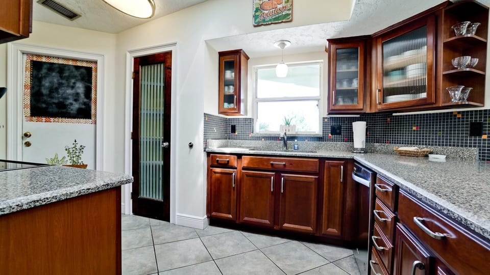 Kitchen with speckled granite countertops, dark wood cabinets, black mosaic tile backsplash, and a frosted glass door.