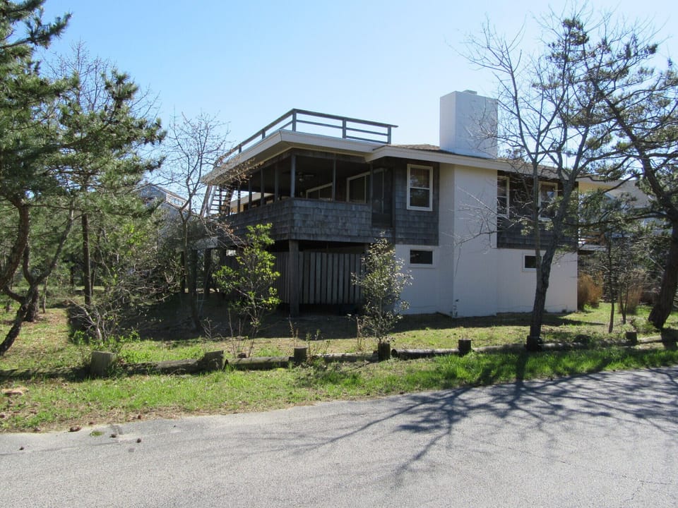29554 N. Dune Way, Cotton Patch, North Bethany - Exterior Side V - A side elevation of the beach house showing the deck structure, exterior siding, and surrounding greenery.