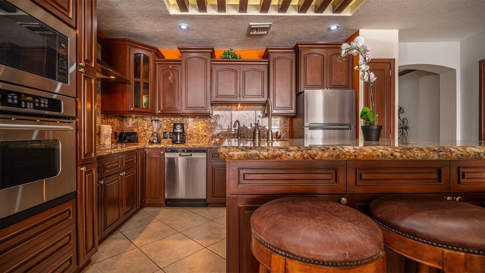 Rich decor continues into the kitchen with fine cabinetry, and full appliances. Note the overhead vigas and recessed lighting.