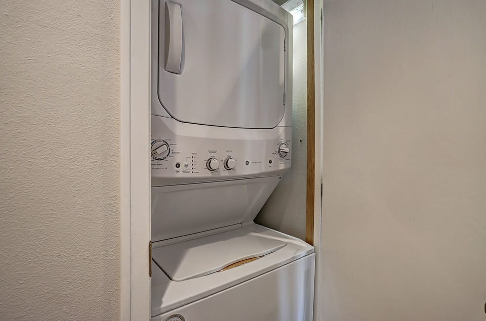 A stacked washer and dryer unit is installed in a small, recessed space within a room.