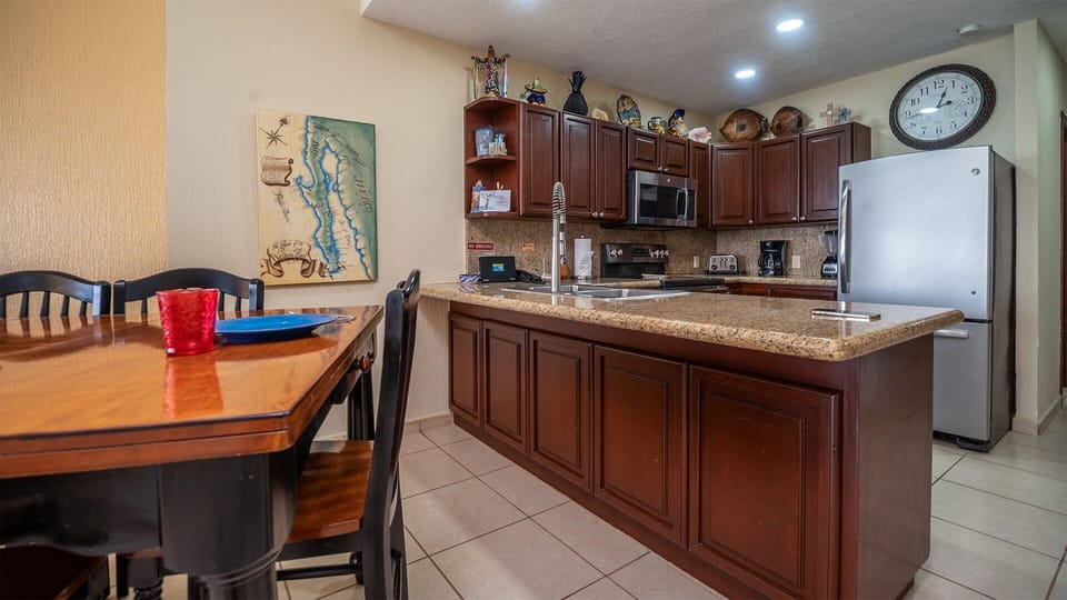 This open-concept space connects the fully equipped kitchen with a classic wooden dining table. Modern stainless steel appliances and rich cabinetry create a warm, functional setting perfect for cooking and gathering.