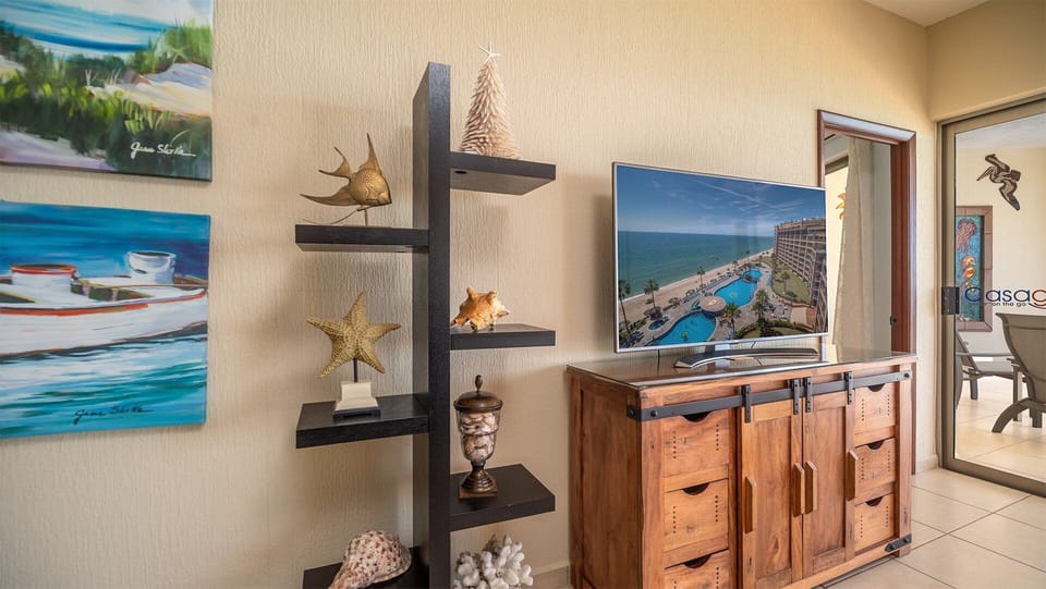 The flat-screen TV sits atop a beautiful wooden console, surrounded by shelves adorned with coastal-inspired décor—bringing a touch of the sea indoors and adding character to the living space.