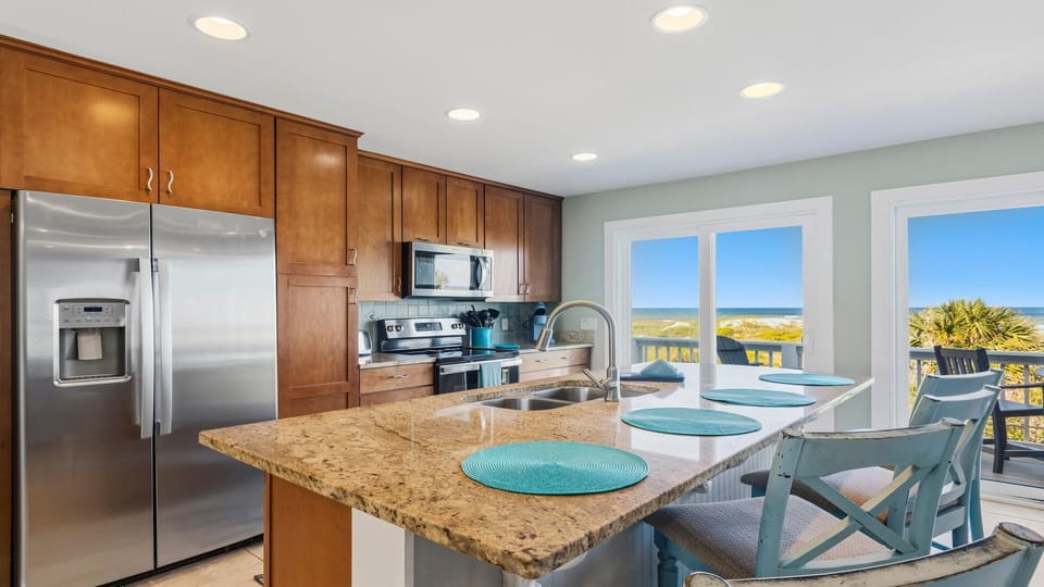 Granite kitchen island with stainless steel sink faces sliding glass doors opening to oceanfront balcony.
