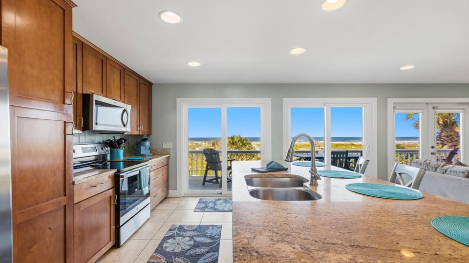 Kitchen island with dual sinks and turquoise placemats faces sliding glass doors opening to oceanfront deck.