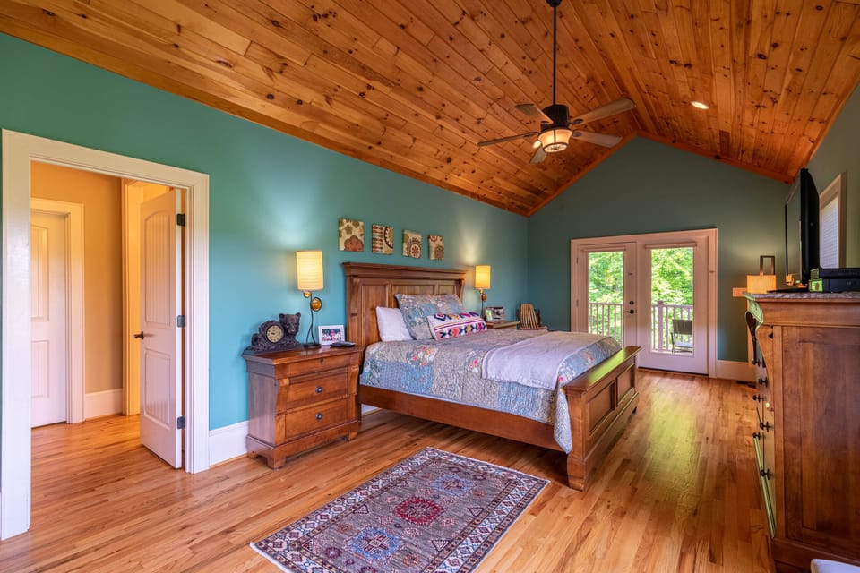Vaulted wood ceilings and teal walls give this master bedroom a cozy yet airy feel, with French doors opening to the treetops beyond.