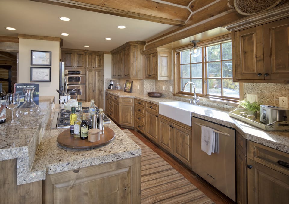 Your gourmet kitchen invites you to create culinary masterpieces with its warm wood cabinetry, granite countertops, and farmhouse sink overlooking serene views through expansive windows.