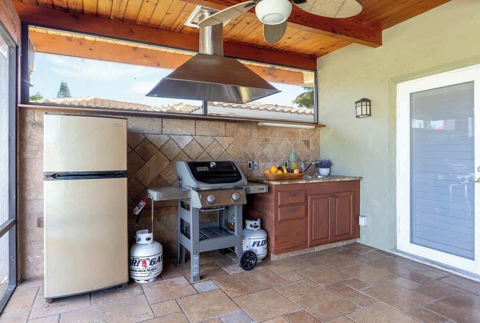 An outdoor kitchen with a refrigerator, gas grill, and sink