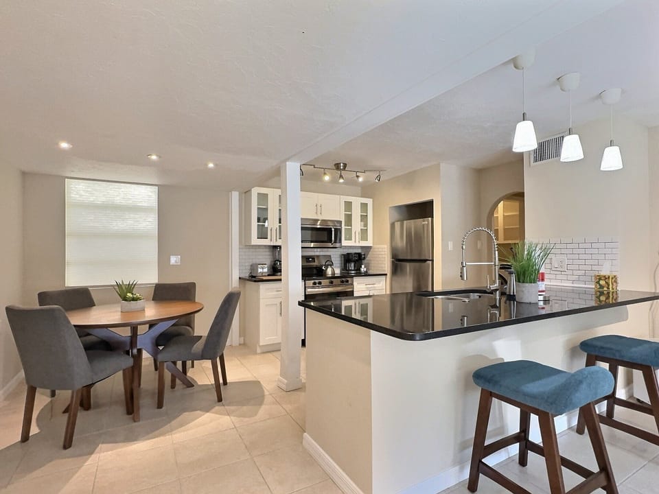 The dining area offers a table for four and an extended breakfast bar in the fully equipped kitchen with stainless steel appliances and a stone-gray tile backsplash.
