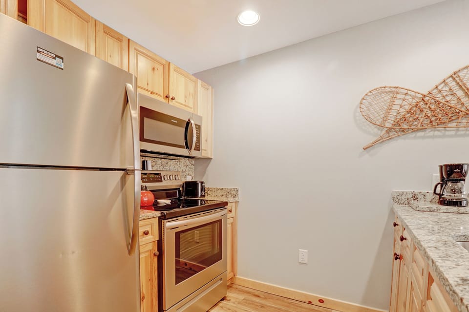 Your fully equipped kitchen awaits with warm wood cabinets, granite counters, and stainless steel appliances - perfect for preparing meals while you enjoy the cozy mountain retreat atmosphere.