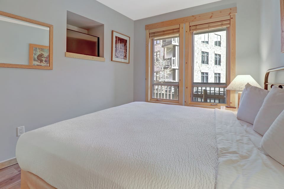 Wake up to city views from your cozy bedroom where natural light streams through charming wooden-framed windows. The crisp white linens and peaceful atmosphere create the perfect retreat.