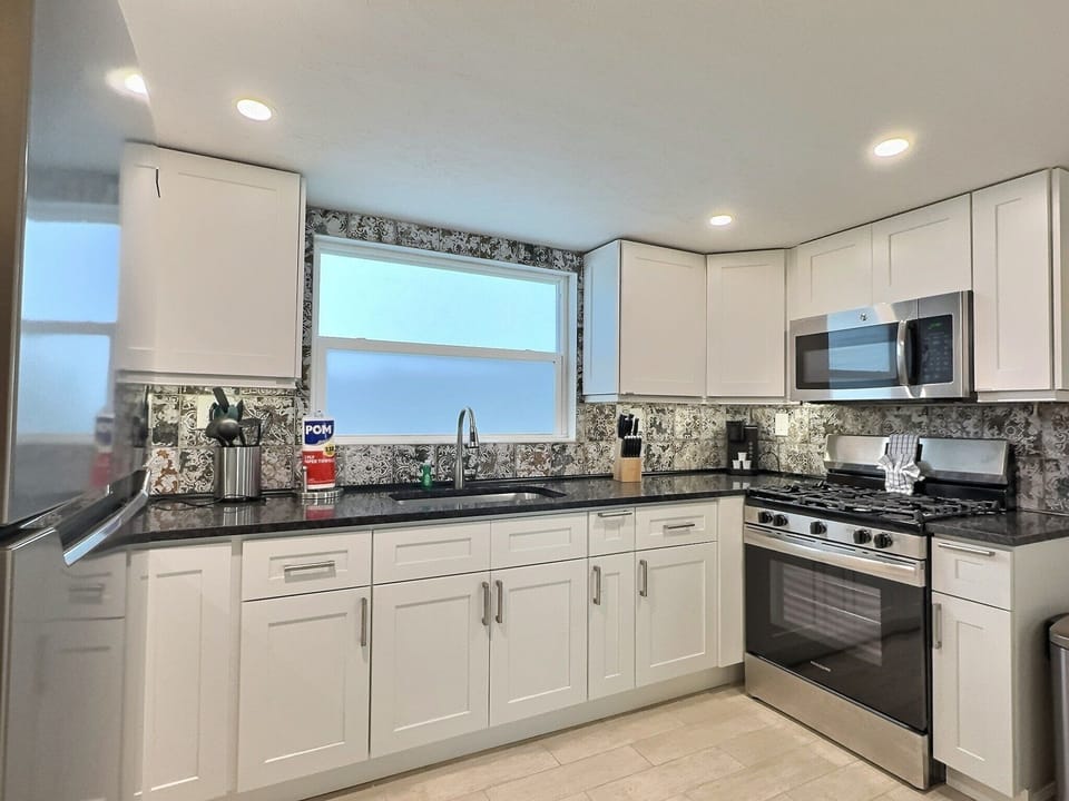 Kitchen with dark stone countertops, gas range, microwave, and white cabinets