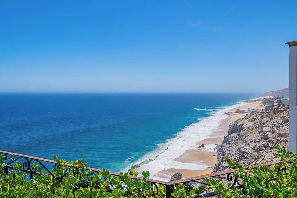 The property overlooks a dramatic coastline where golden sands meet turquoise waters, framed by rugged cliffs stretching along the horizon.