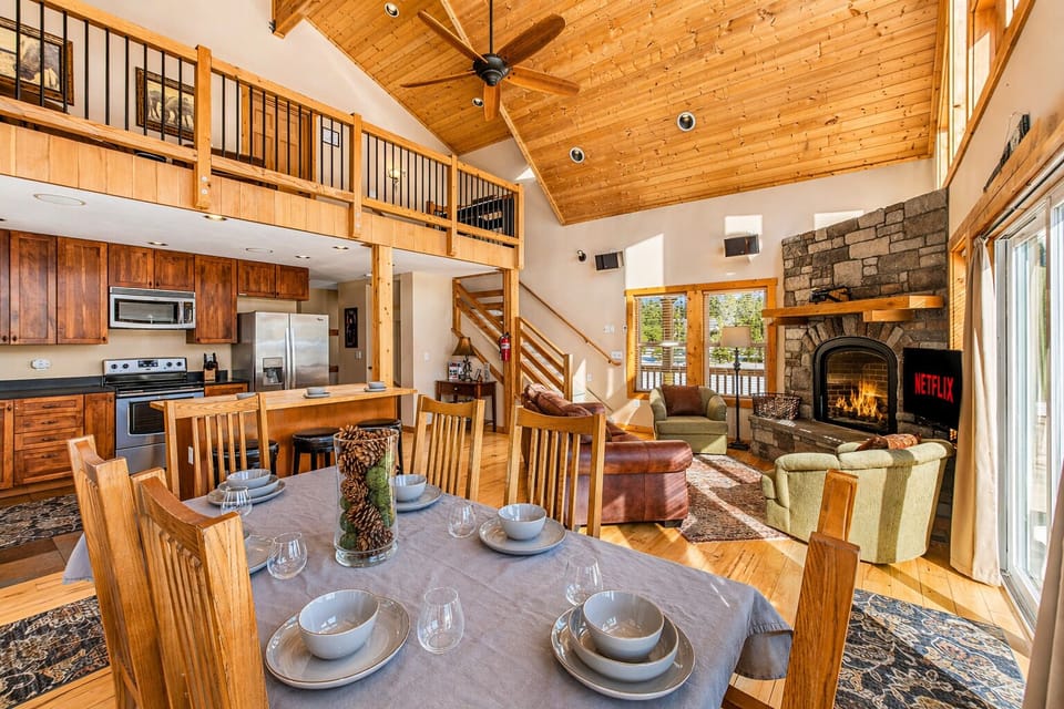 Gather around the dining table where warm wood meets cozy stone fireplace, creating your perfect mountain retreat atmosphere.