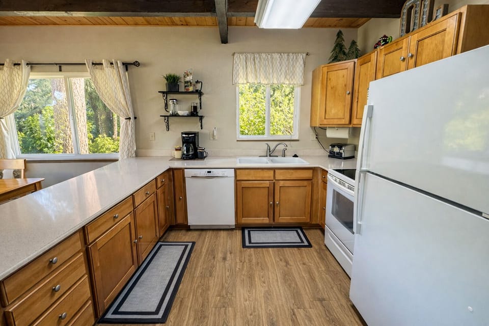 Your fully-equipped kitchen awaits with warm wood cabinetry, modern appliances, and peaceful garden views through charming windows.