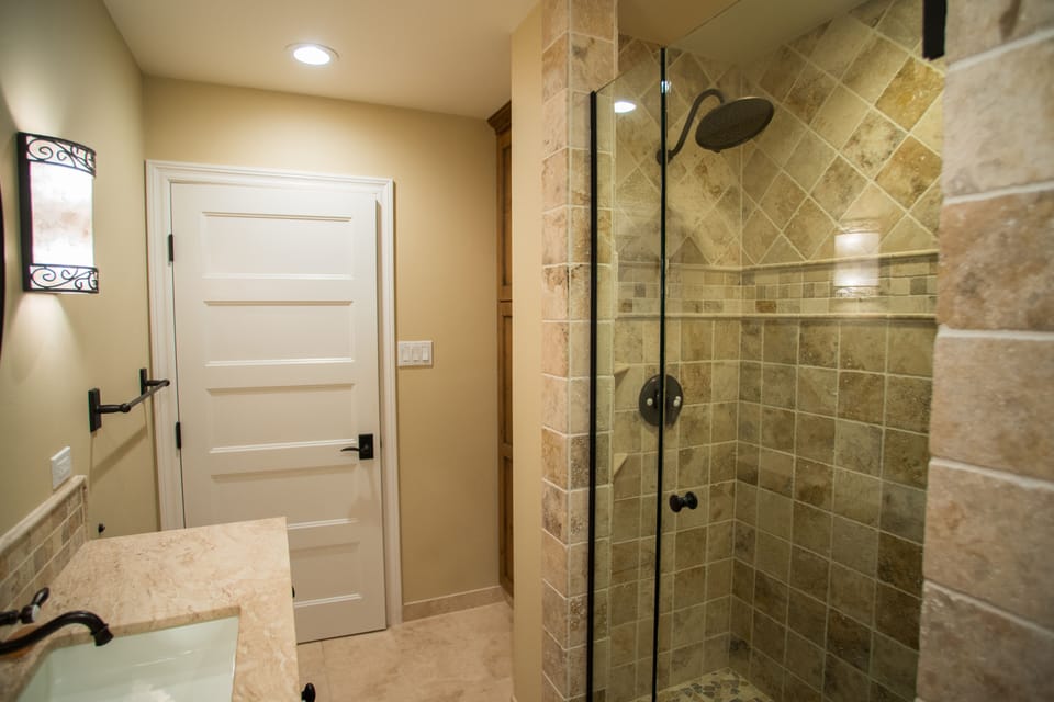 A full bathroom with a glass-enclosed walk-in shower and textured stone tile.